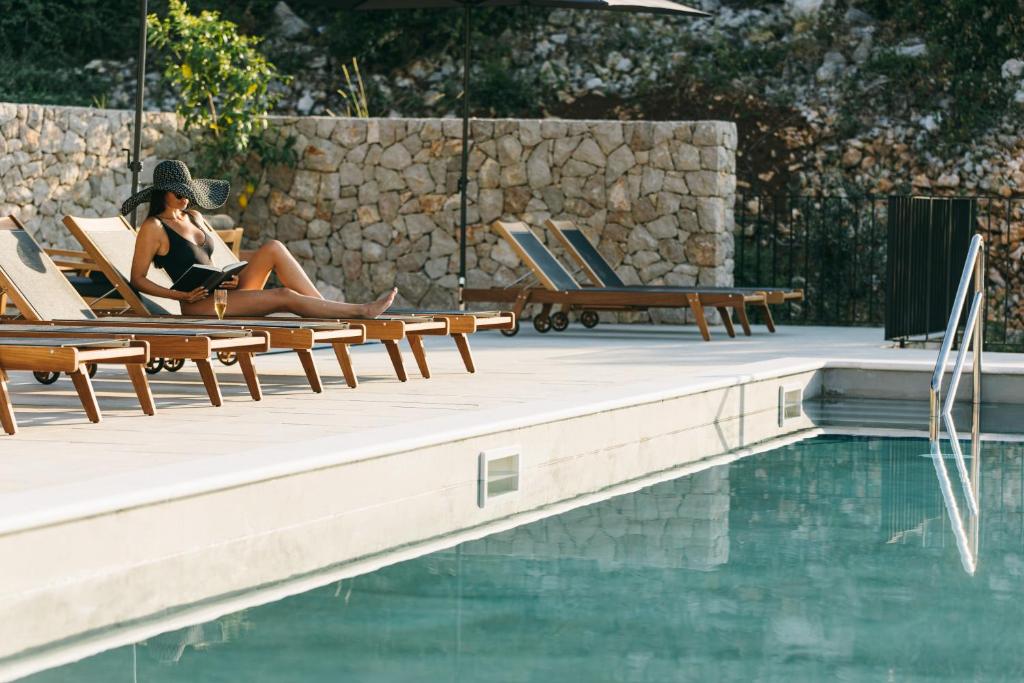 a woman sitting in lounge chairs next to a swimming pool at DESIGN hotel VERBENICUM in Vrbnik