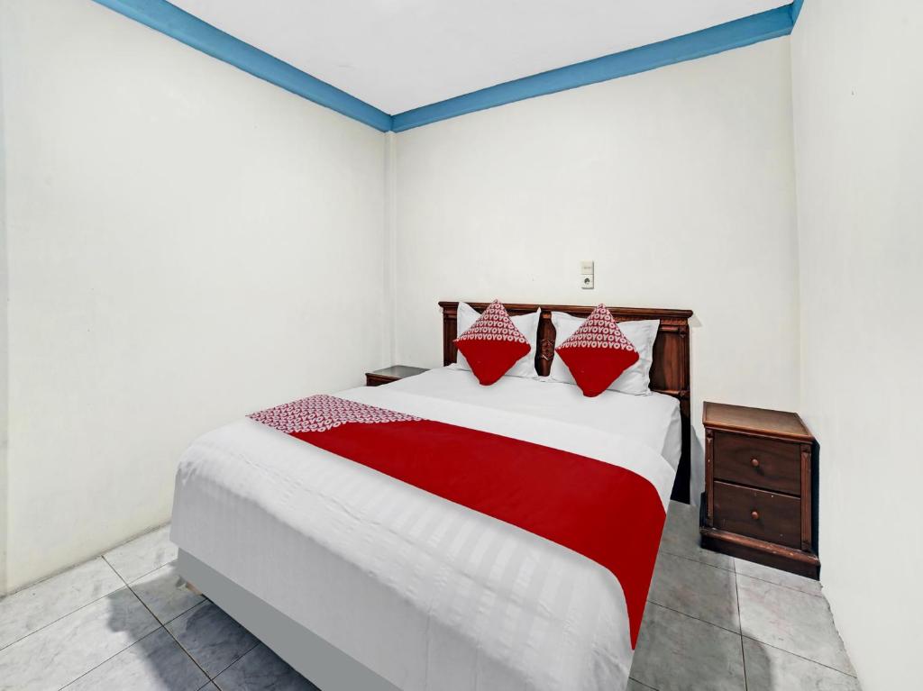 Hagu的住宿－OYO 90487 Wisma Kuta Karang Baru，一间卧室配有一张带红色和白色床单的大床