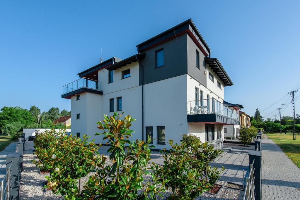 a white house with a balcony and some bushes at Theresa Vendégház in Kiskunmajsa