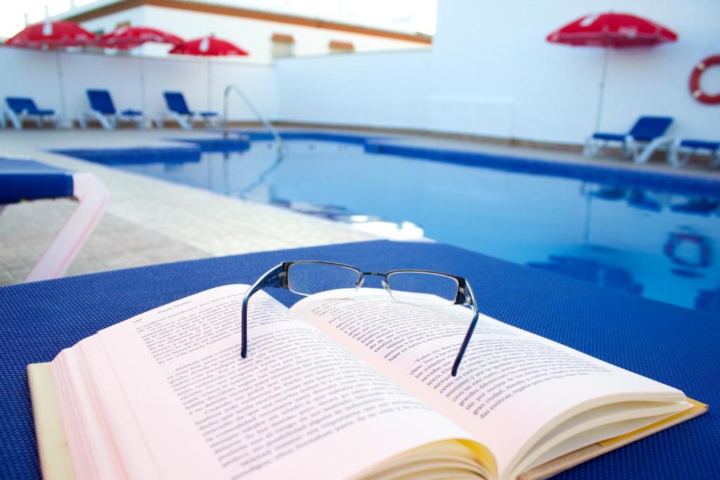 een boek met glazen op een tafel naast een zwembad bij Villa la Dehesa in Conil de la Frontera