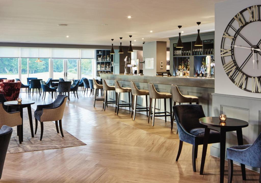 a restaurant with a bar with chairs and a large clock at Formby Hall Golf Resort & Spa in Southport