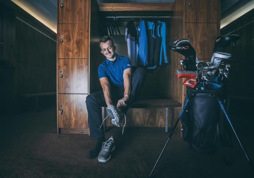 a man sitting on a bench in a closet with his shoes at Formby Hall Golf Resort & Spa in Southport