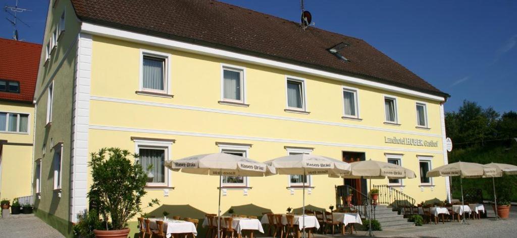 um edifício amarelo com mesas e guarda-chuvas à sua frente em Landhotel Gasthof Huber em Merching