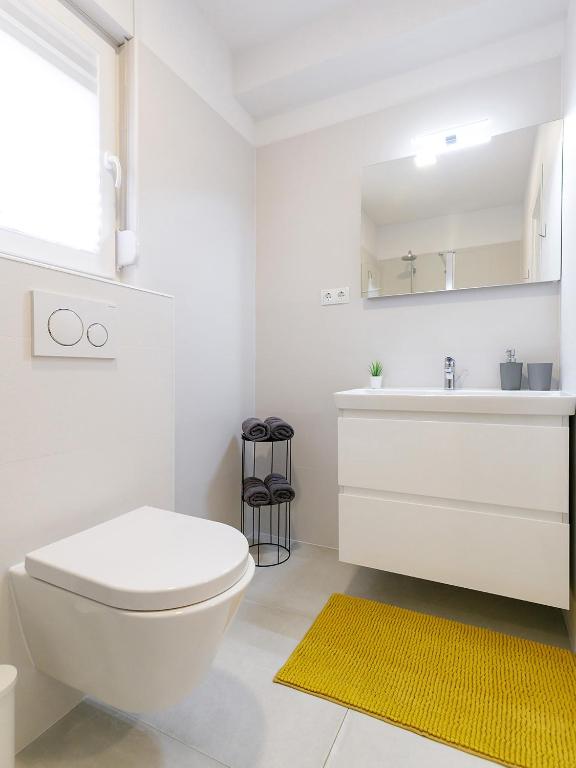a white bathroom with a white toilet and a yellow rug at Apartment Aria in Poreč