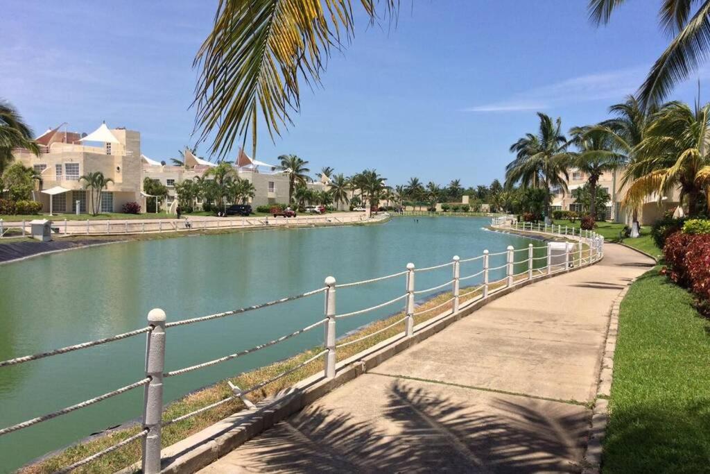 une passerelle à côté d'une étendue d'eau plantée de palmiers dans l'établissement Depa Frente al Mar en Acapulco Diamante, à Acapulco