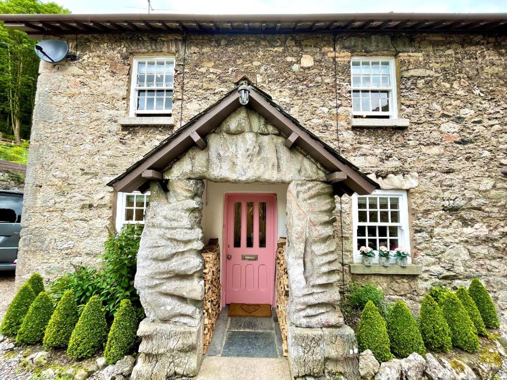 uma casa de pedra com uma porta rosa à frente em Pear Tree Cottage em Grange Over Sands