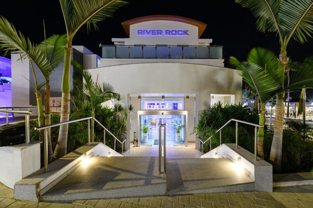 a white building with stairs and palm trees at night at River Rock Hotel in Ayia Napa