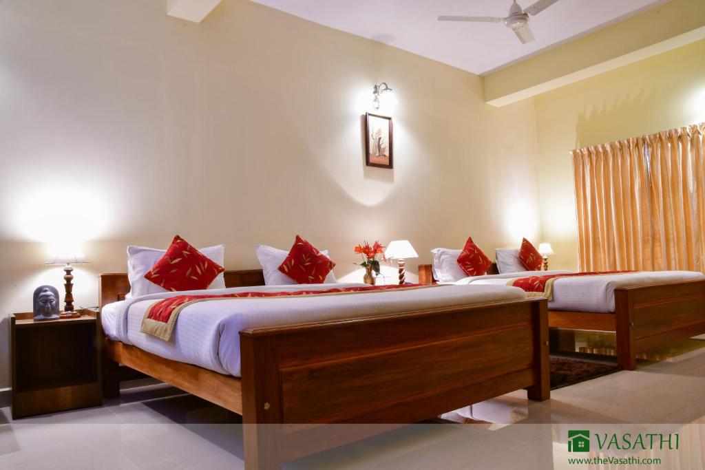 a bedroom with two beds with red pillows at Vasathi in Madikeri