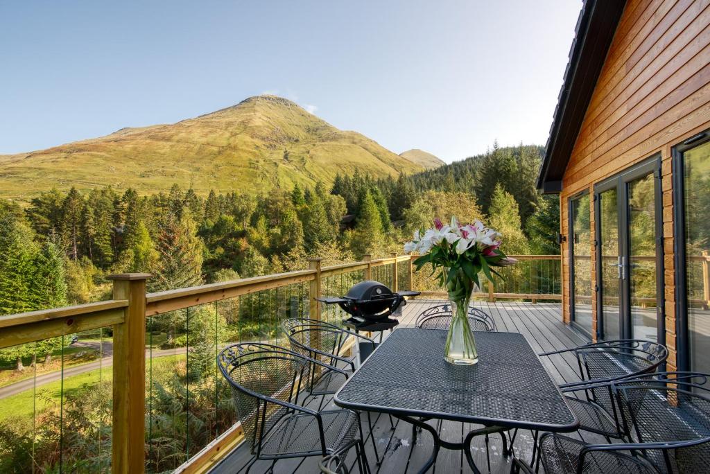 a table with chairs and a vase of flowers on a balcony at Stunning 5 star chalet with loch views in Crianlarich