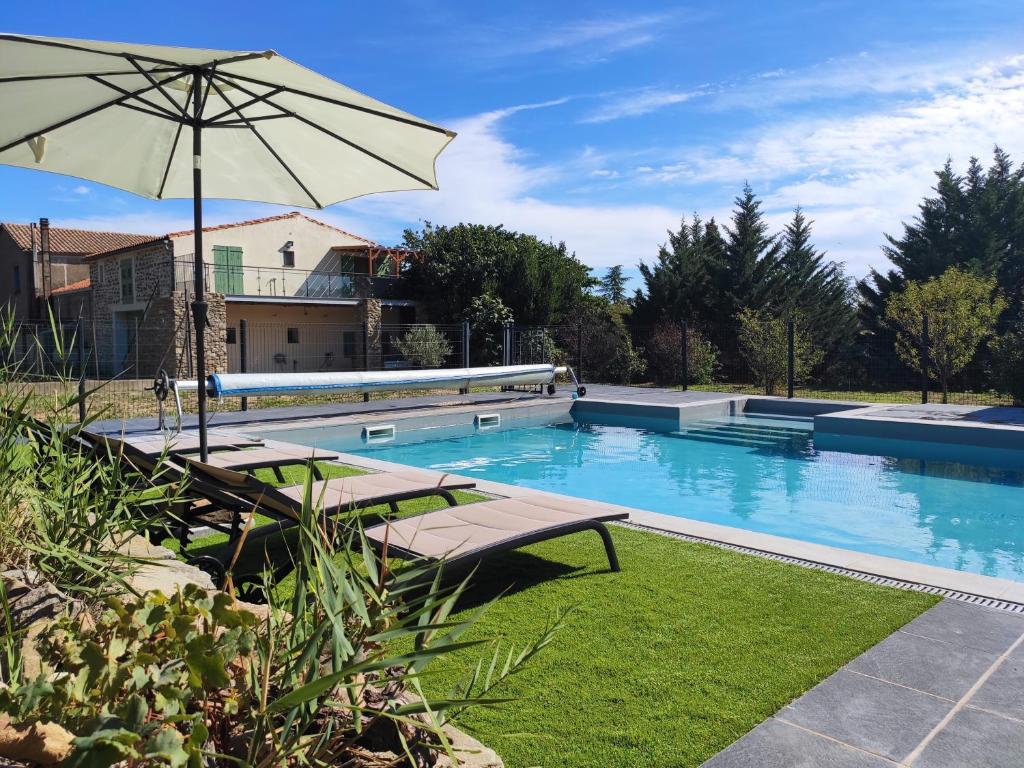 a swimming pool with benches and an umbrella at Domaine d'Azéou in Laure-Minervois