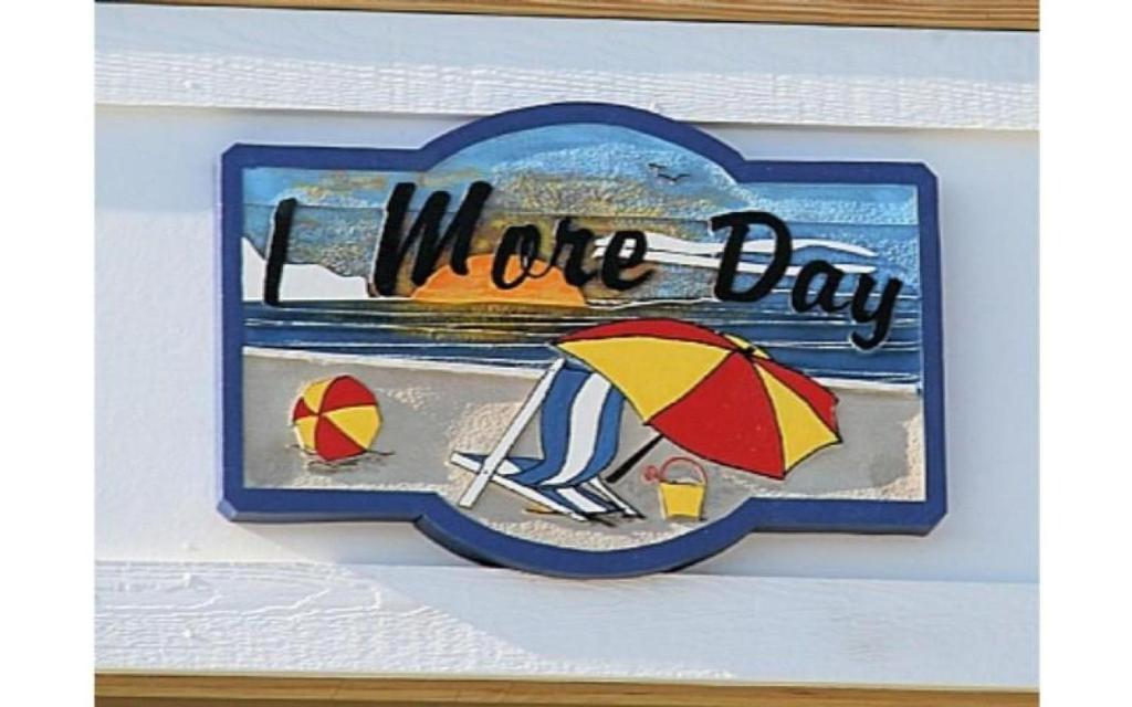 a sign with a picture of a beach with an umbrella at 1 More Day in Oak Island