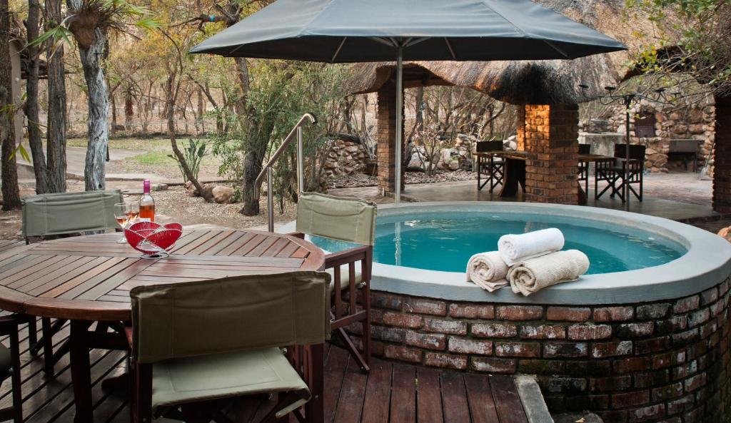 bañera de hidromasaje con mesa, sillas y sombrilla en De Bruine Huis, en Marloth Park