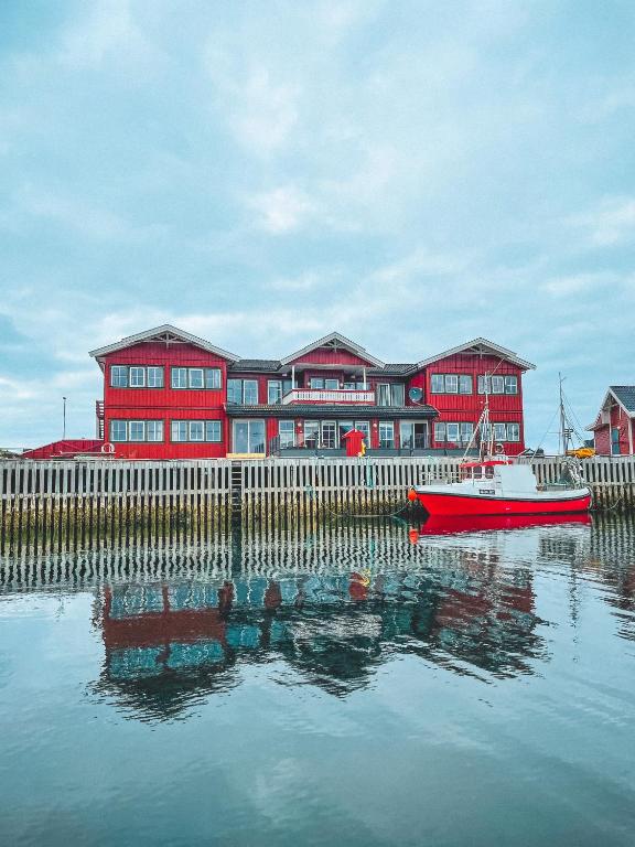 a red building with a red boat in the water at Røst Bryggehotell in Røst