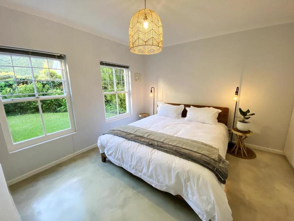 a bedroom with a large bed and two windows at Daisy Cottage in Hermanus