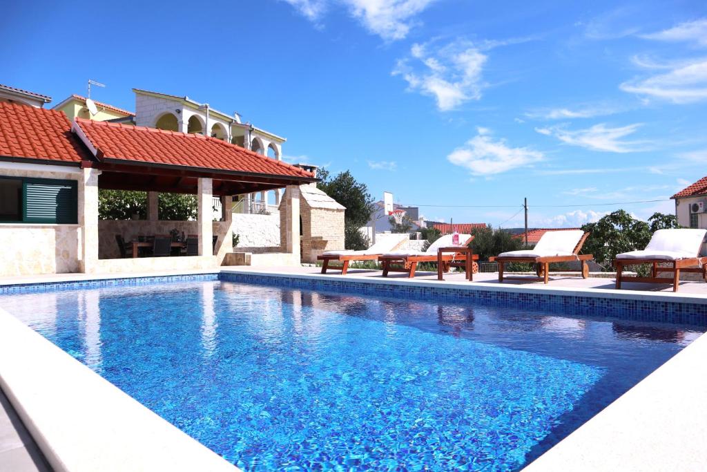 a swimming pool with chairs and a house at Restful Kanica House in Rogoznica