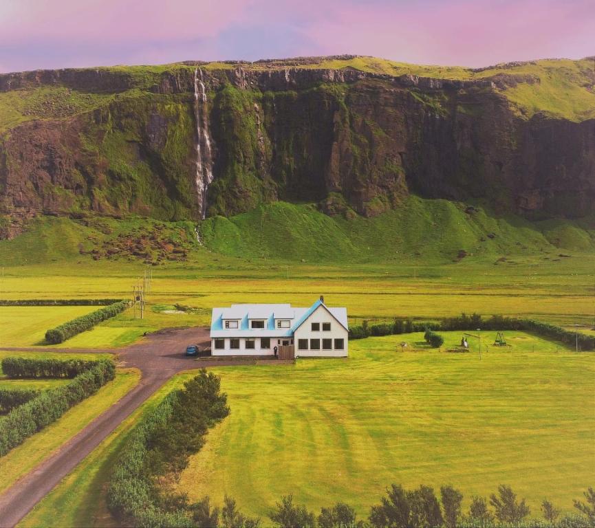 a house in the middle of a field with a waterfall at Paradise Cave Hostel & Guesthouse in Hvolsvöllur