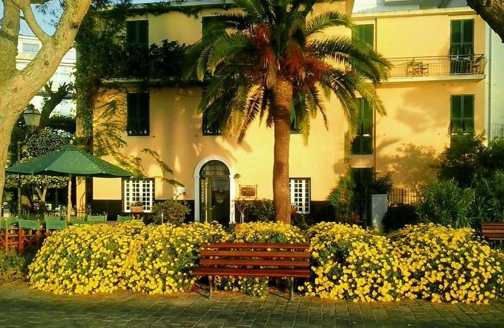 um banco de parque em frente a um edifício com flores amarelas em Hotel Beau Rivage em Alassio