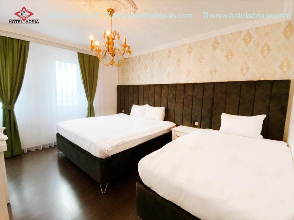 a hotel room with two beds and a chandelier at Hotel Adria in Pristina