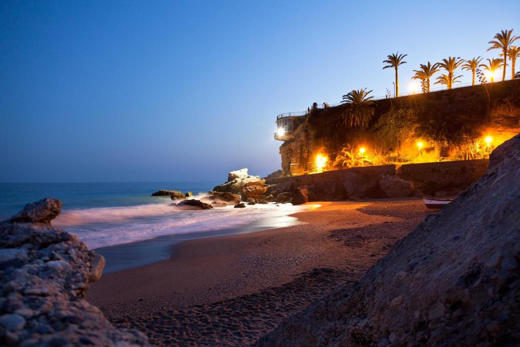 a beach with palm trees and the ocean at night at AT Almoraide Rooms Suites in Nerja