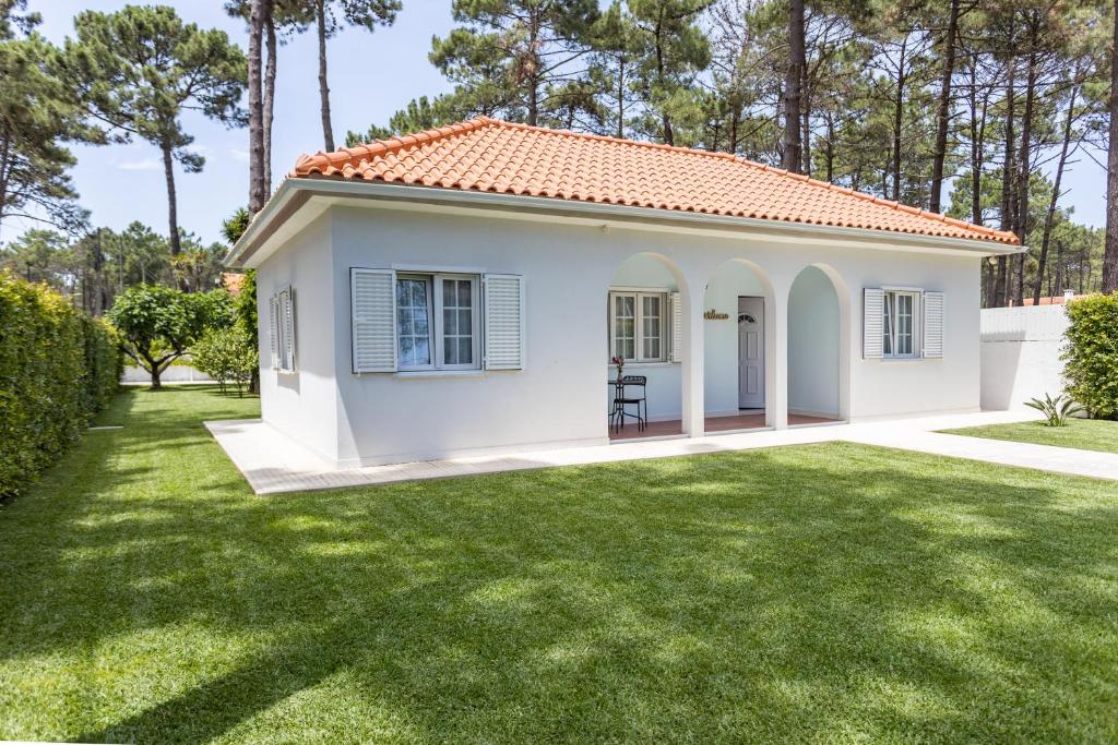 ein kleines weißes Haus mit einem Rasenhof in der Unterkunft CASA AROEIRA - Beach bungalow near Lisbon in Charneca