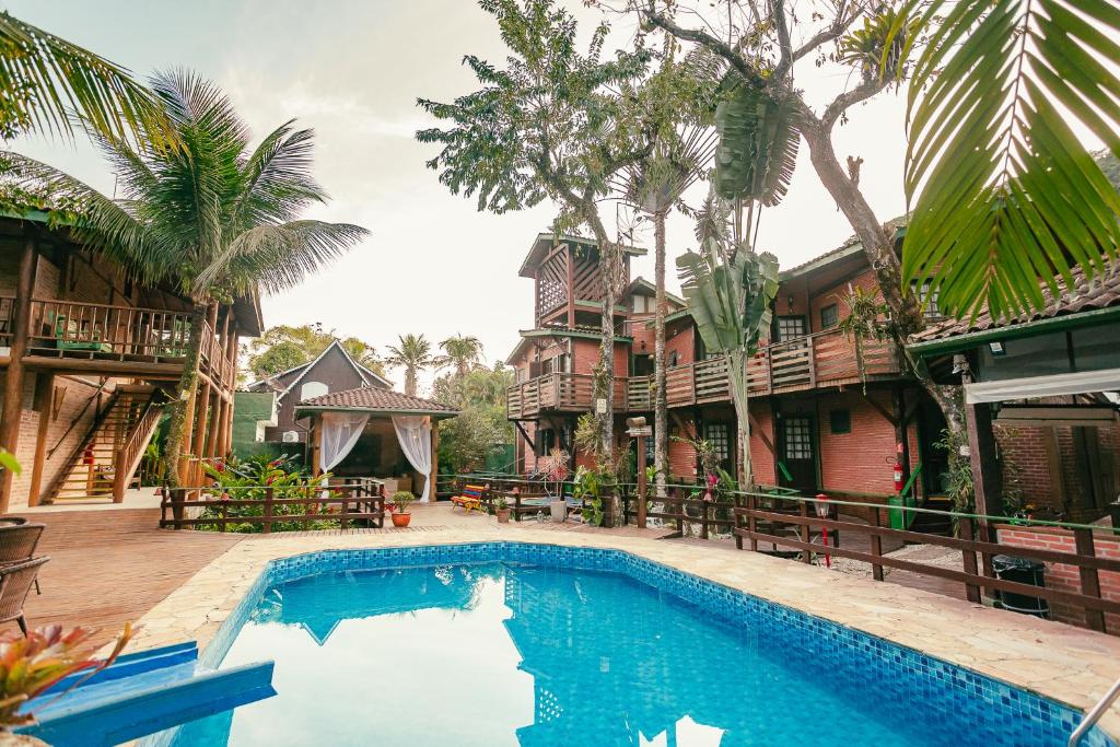 a swimming pool in front of a house with trees at Pousada Maná in Boicucanga