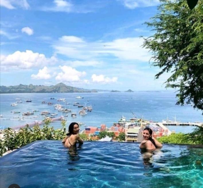 two women in a swimming pool with a view of the ocean at Bayview Gardens Hotel in Labuan Bajo