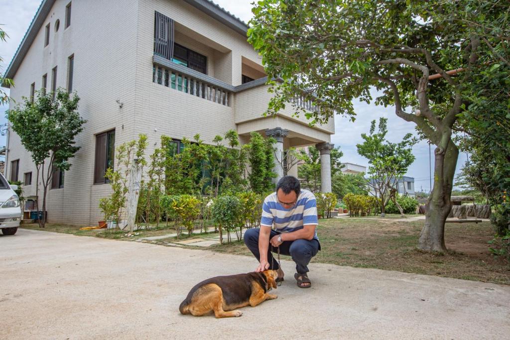 a man petting a dog in front of a house at 金門自由行民宿 Kinmentrip B&amp;B in Jincheng