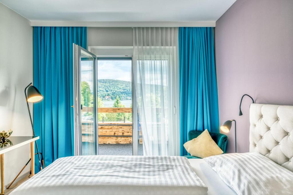 a bedroom with blue curtains and a bed and a balcony at Hotel Eden Park in Velden am Wörthersee