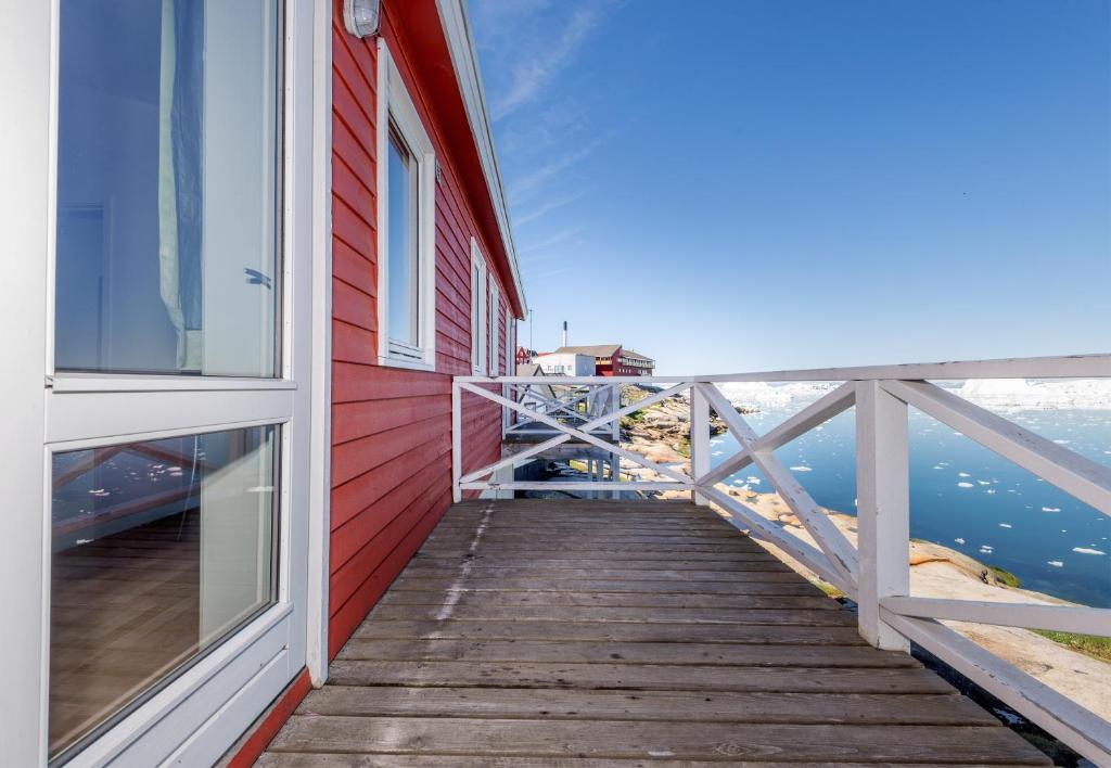 a red building with a wooden walkway next to a window at Hotel Hvide Falk in Ilulissat