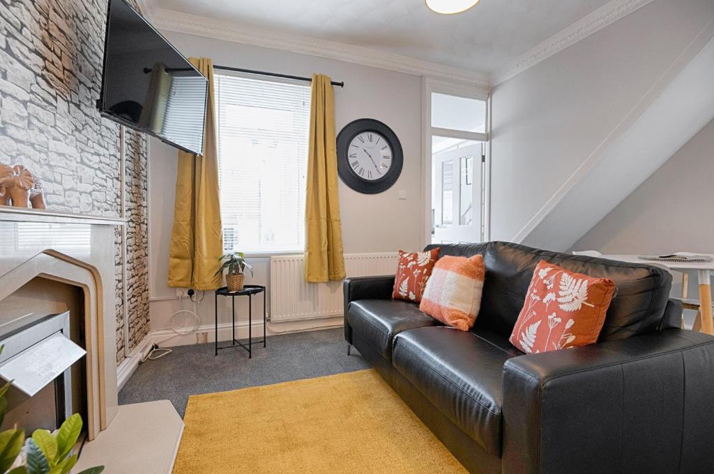 un sofá de cuero negro en una sala de estar con reloj en Crymlyn Accommodation - TV in Every Bedroom! en Swansea