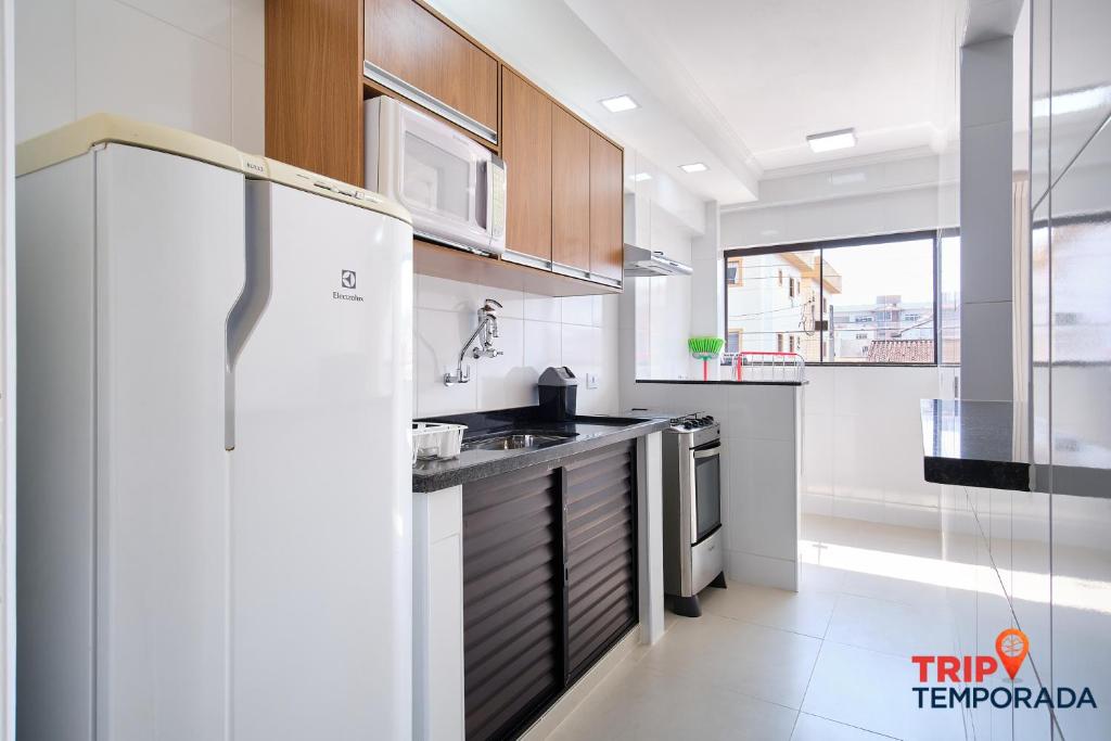 a white kitchen with a refrigerator and a sink at Apartamento com ar condicionado à 100 metros da praia - Edifício Ibiza in Ubatuba