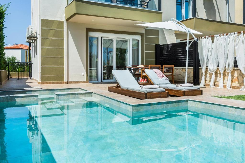 - une piscine avec 2 chaises et un parasol dans l'établissement SPA Villa - Sunny Villas Hanioti, à Chaniotis