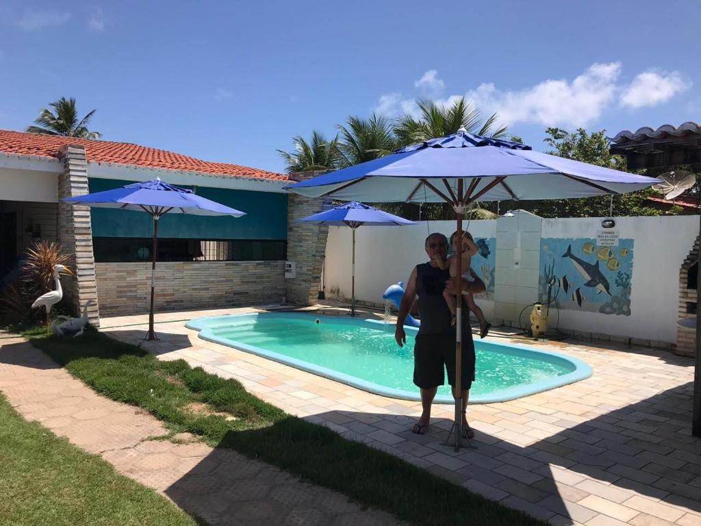 a man holding a child under an umbrella next to a pool at CASA TEMPORADA SÃO JOSE DA COROA GRANDE - PE in São José da Coroa Grande