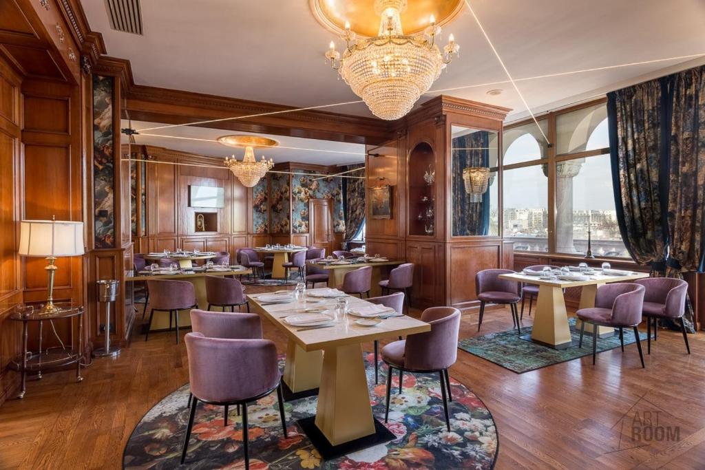 Wood-paneled dining room with purple upholstered chairs, set tables, floral banquette and large arched windows with city view at Suter Palace Heritage Boutique Hotel in Bucharest
