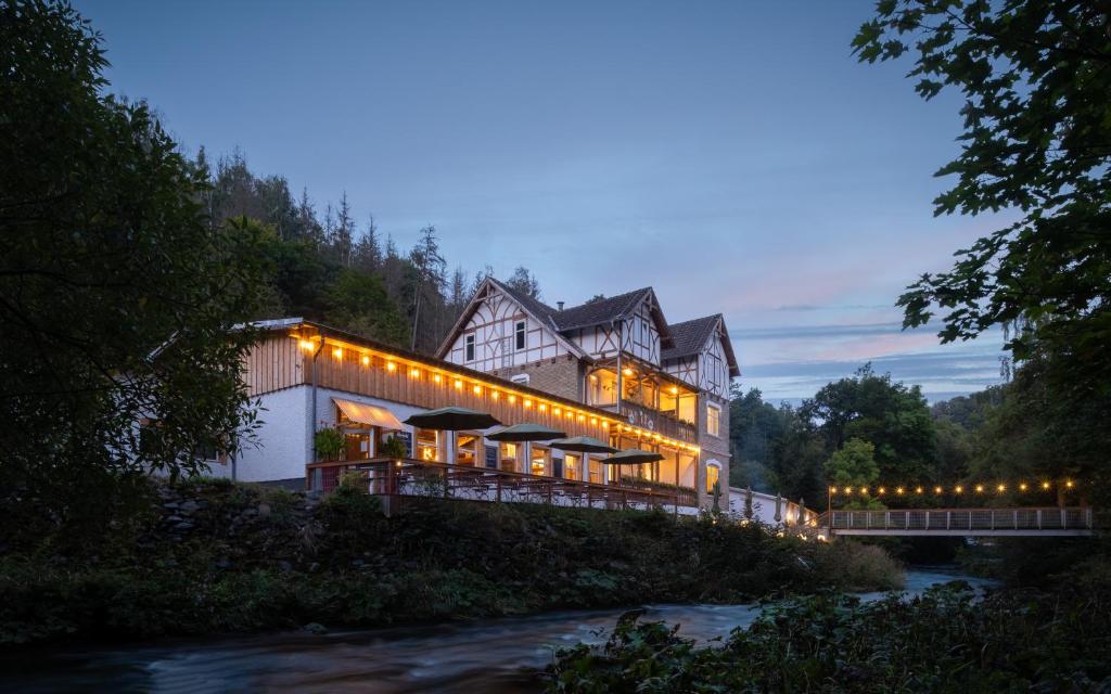 uma casa grande com luzes ao lado de um rio em BODETALER BASECAMP LODGE - Bergsport- und Naturerlebnishotel em Rübeland