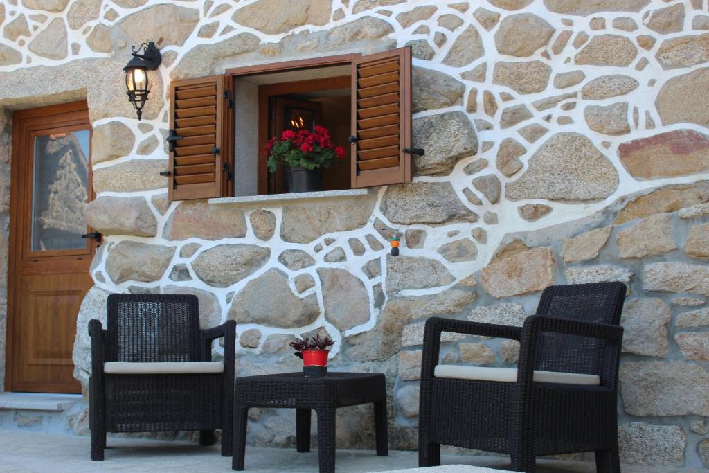 two chairs and a table in front of a stone wall at Suite das Fraguinhas in Sistelo