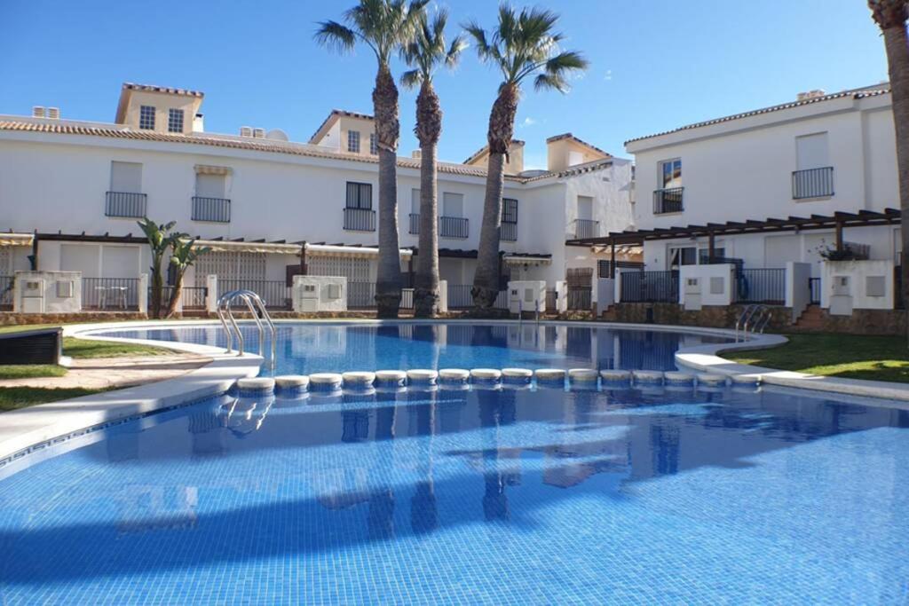 a swimming pool in front of a building with palm trees at Bonrepòs Palm Beach casa adosada en la playa in Alcossebre