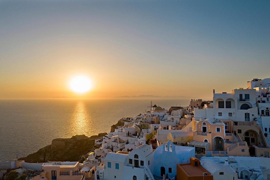a sunset over a town with white buildings and the ocean at Sole d'oro Sunset & Caldera View Grand Suite in Oia