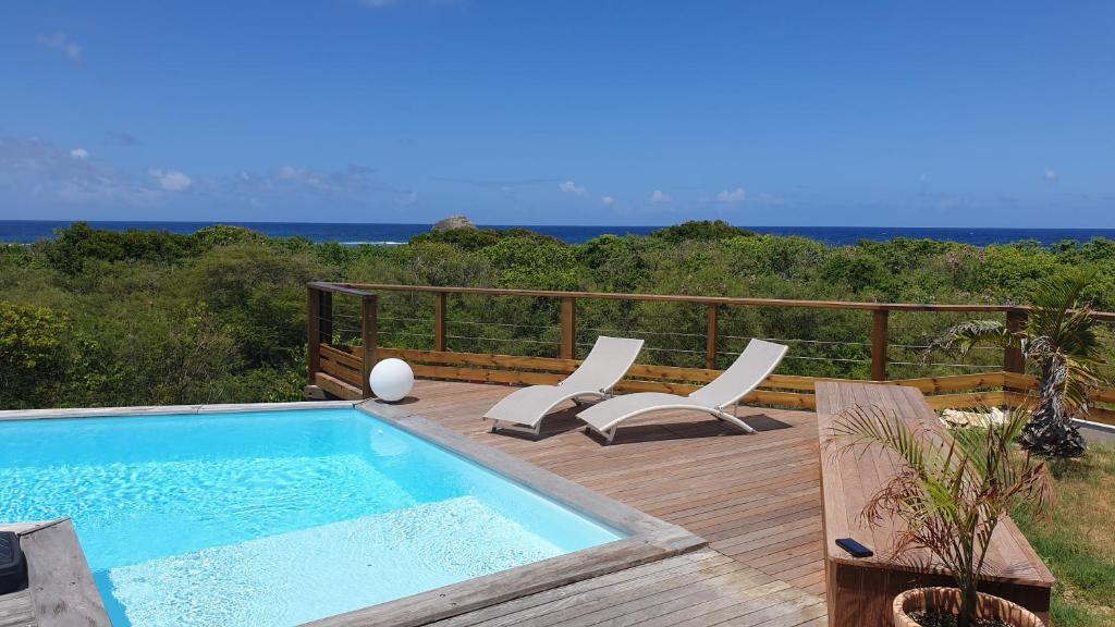 a swimming pool on a deck with chairs and the ocean at Villa Tarare in Kahouanne