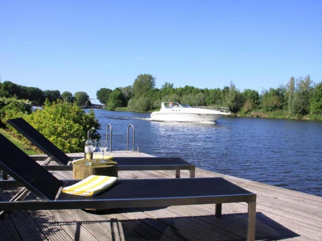 a dock with two chairs and a boat on the water at Riverside holiday home near Amsterdam in Nigtevecht