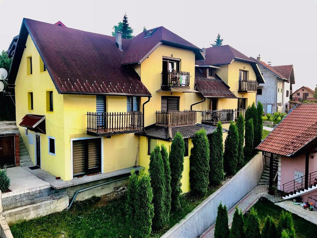 ein gelbes Haus mit einer Reihe von Bäumen davor in der Unterkunft Apartman Gradina Zlatibor in Zlatibor