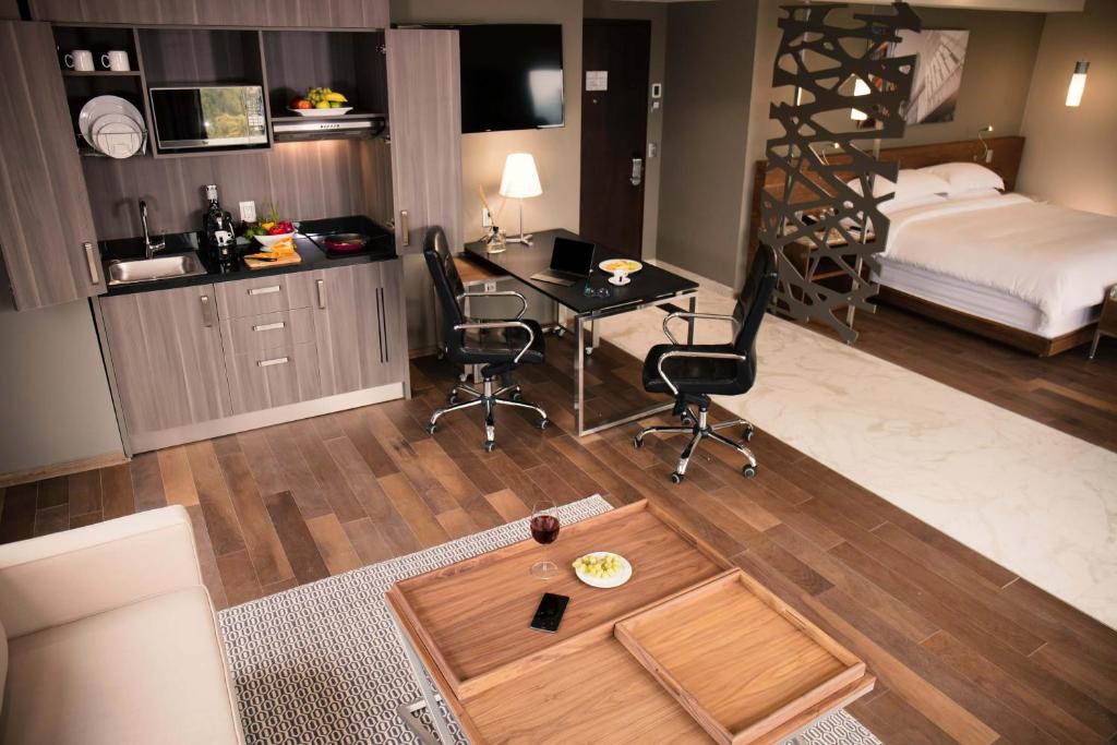 An open-plan suite with a kitchenette, work area, lounge, and partially screened sleeping zone.