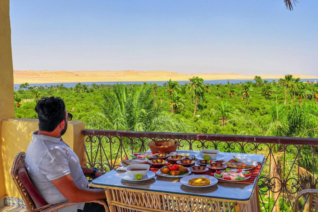a man sitting at a table with food on a balcony at Tache Boutique Hotel Fayoum in Fayoum Center