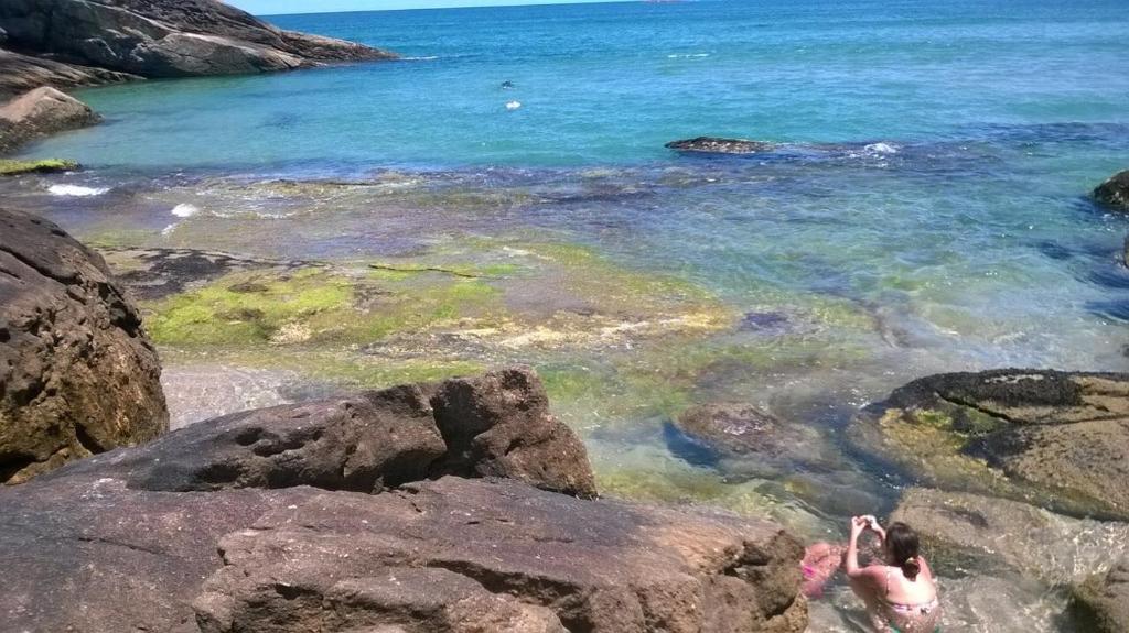 a person standing on some rocks in the water at Suites Praia de Pernambuco in Guarujá