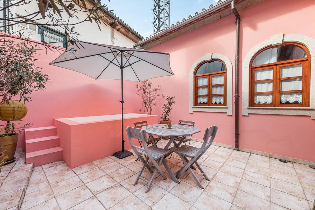 ein rosafarbenes Haus mit einem Tisch, Stühlen und einem Sonnenschirm in der Unterkunft Praça Guest House in Arouca