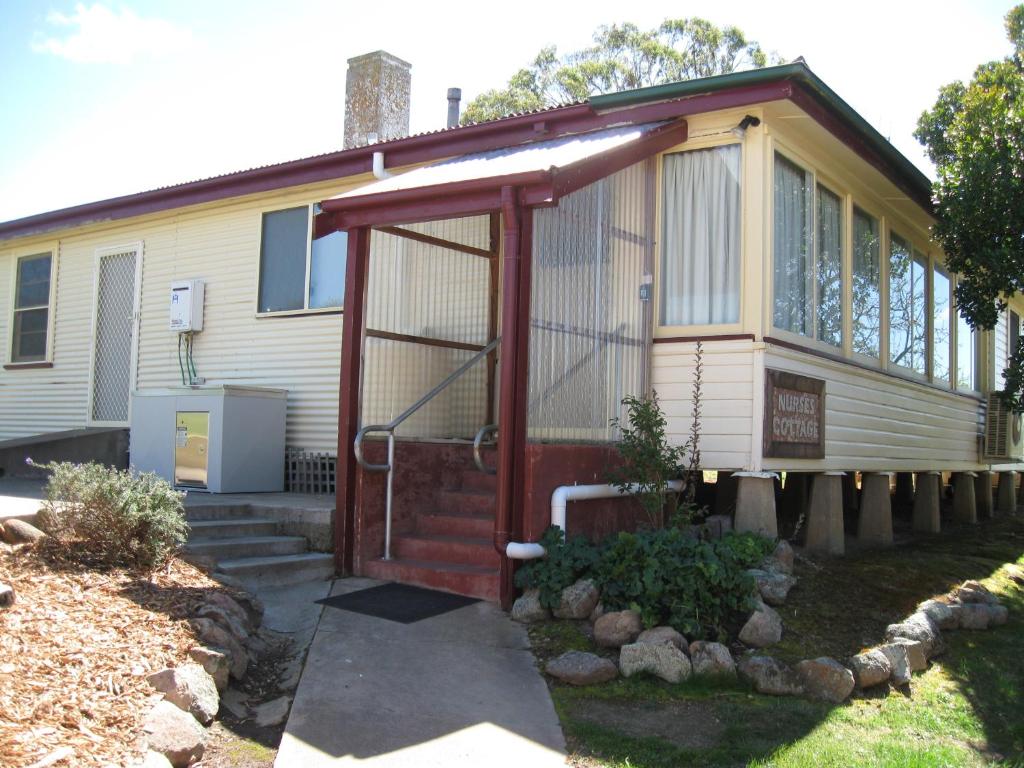 una pequeña casa con una puerta roja delante de ella en Delegate Nurses Cottage, en Delegate