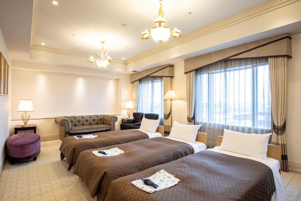 東京にあるホテルカデンツァ東京のベッド2台とソファが備わるホテルルームです。