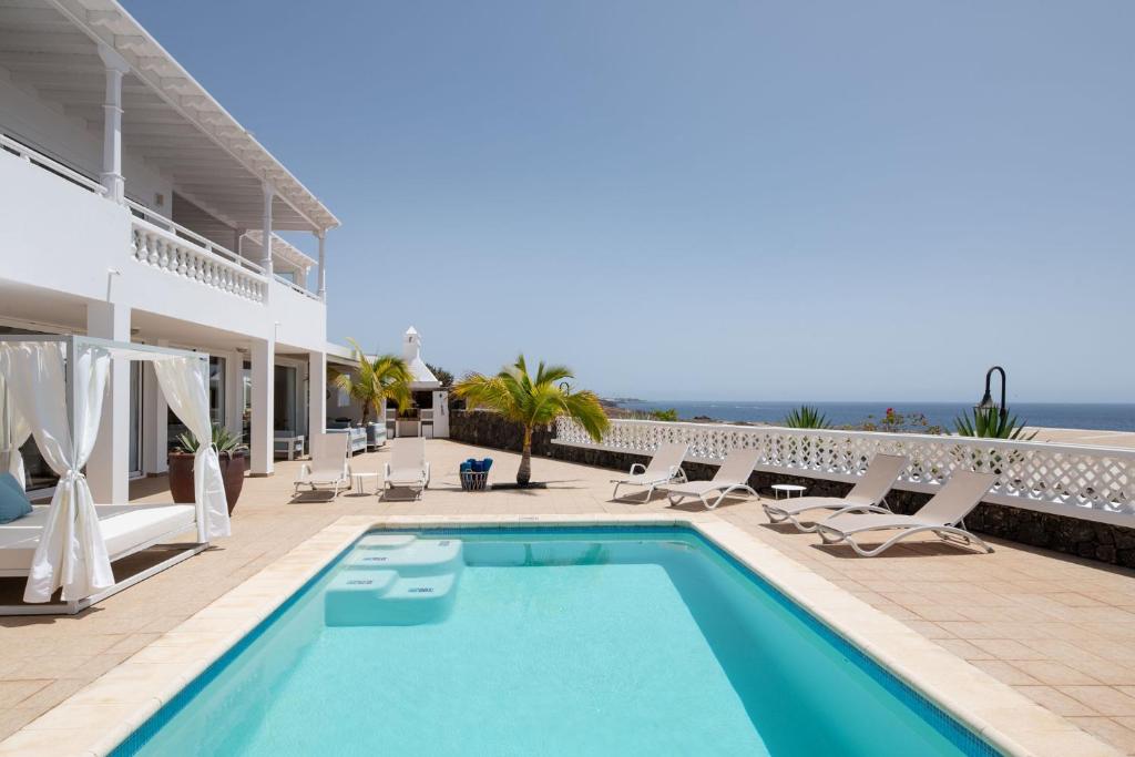 einen Pool mit Stühlen und das Meer im Hintergrund in der Unterkunft ODIN LUXURY VILLA by Buenavilla in Puerto Calero