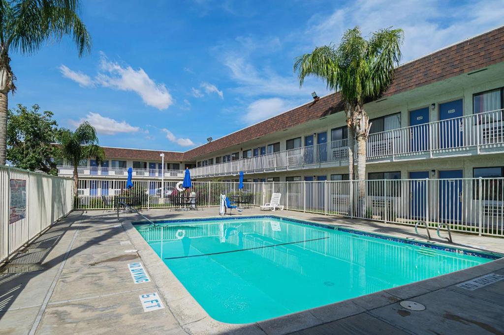a swimming pool in front of a building with palm trees at Motel 6 Lost Hills / Buttonwillow Racetrack in Lost Hills