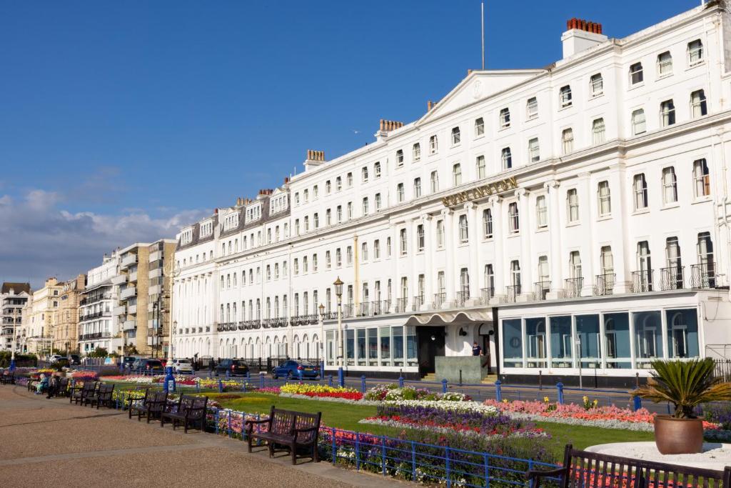 un gran edificio blanco con bancos delante en The Burlington Hotel en Eastbourne